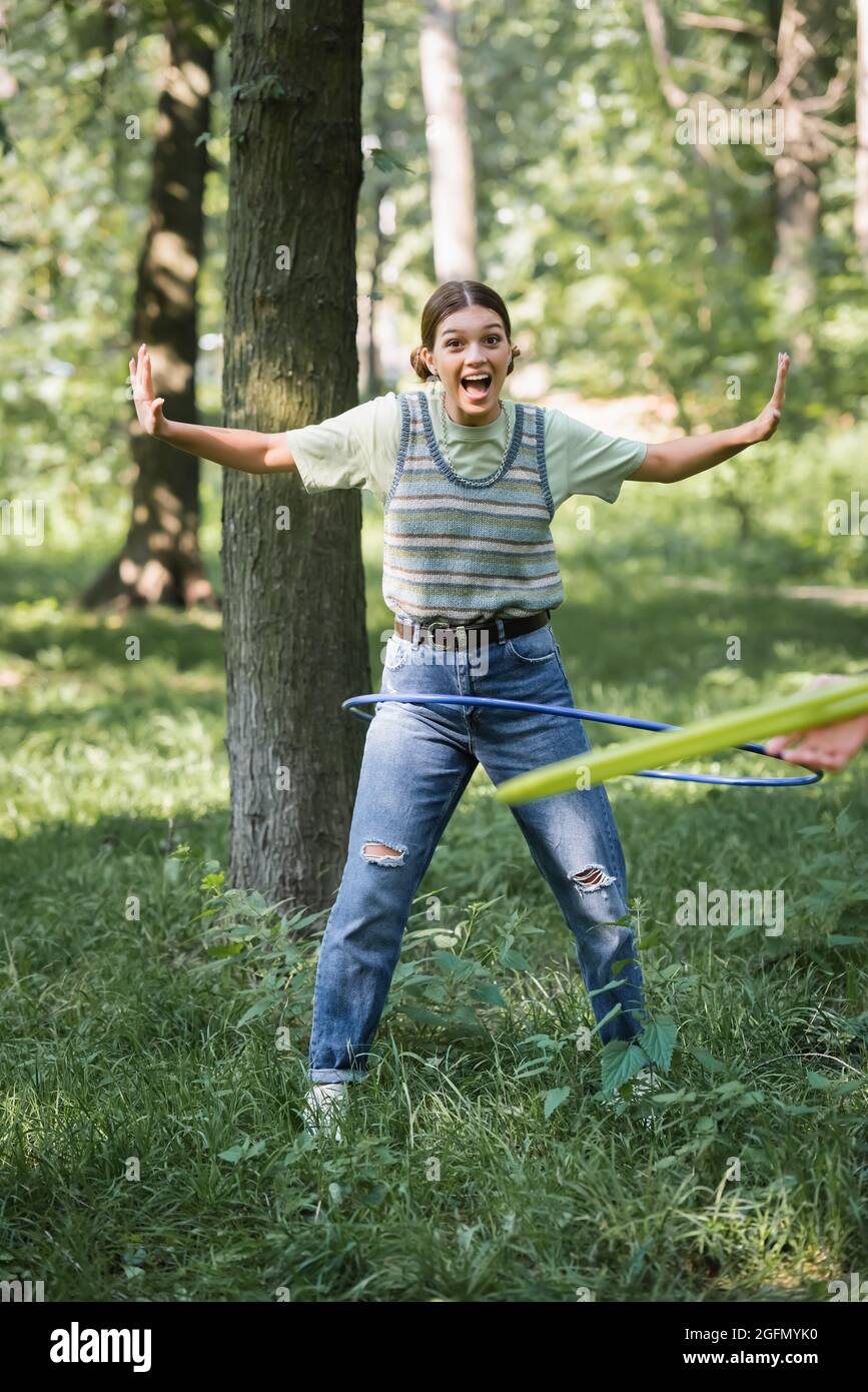 Excited teen girl twisting hula hoop on grass in park Stock Photo