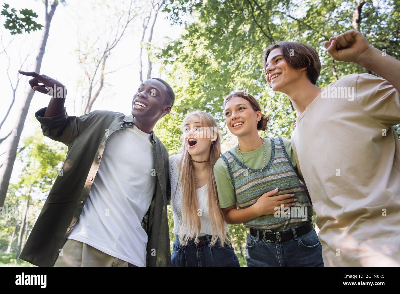 Low angle view of smiling african american boy pointing away near friends outdoors Stock Photo