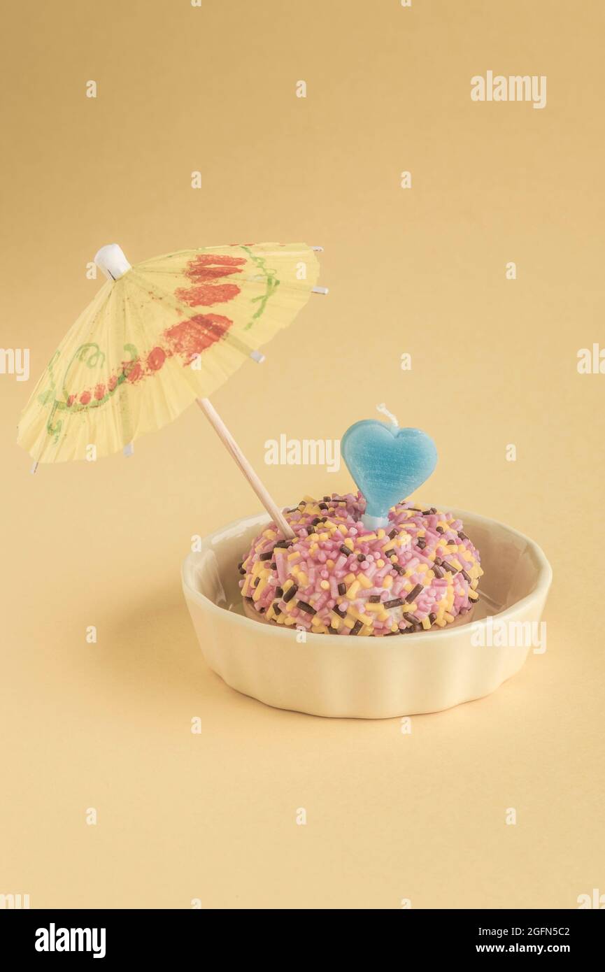 A small birthday cake with heart shaped candle and umbrella on yellow Stock Photo