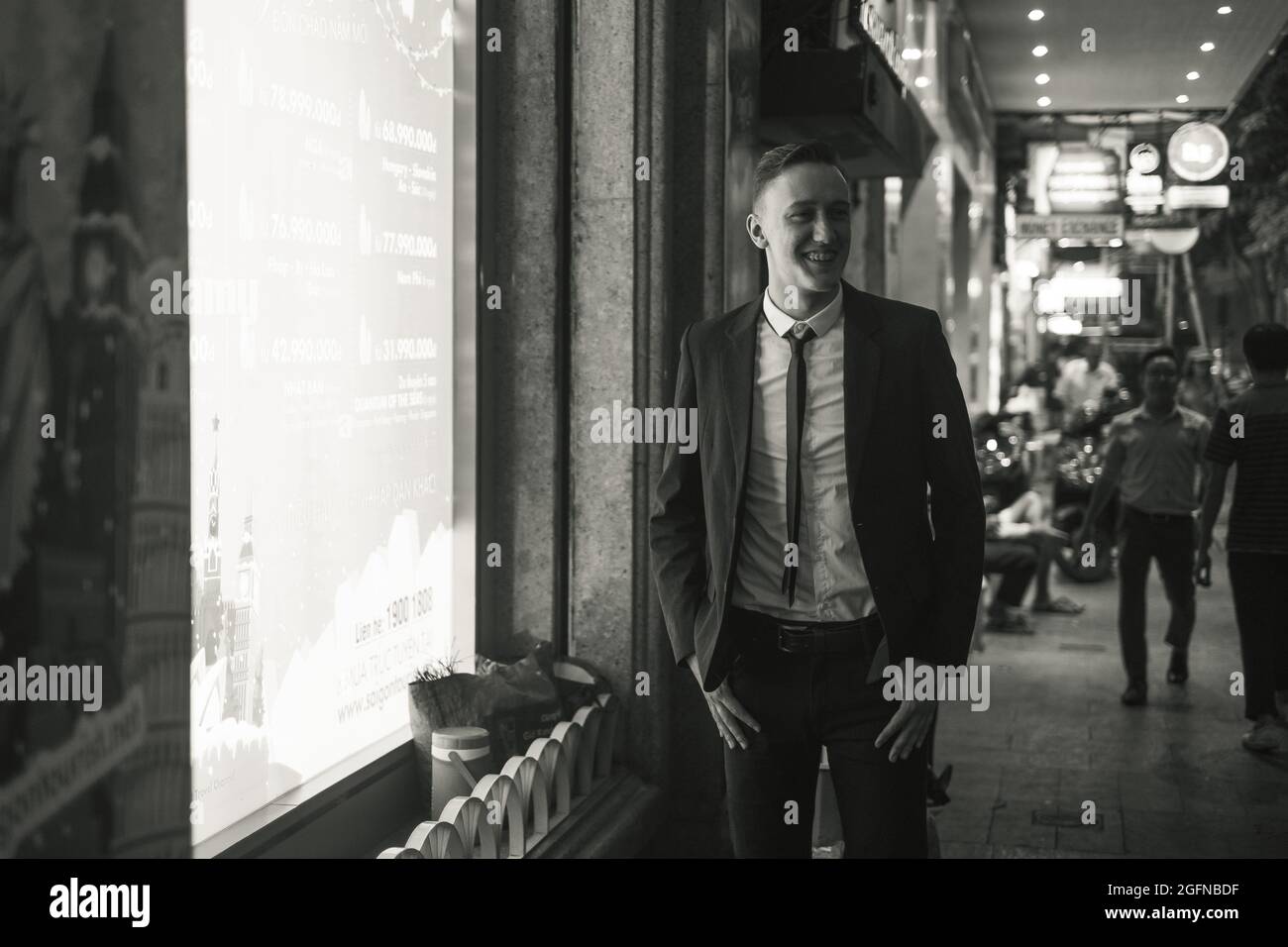 Black and white portrait of young attractive business man in elegant formal suit walking on the street with lights in big city. Night picture. Stock Photo