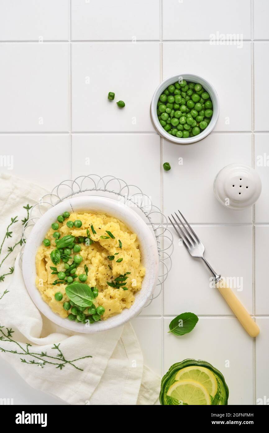 Mashed potato with butter, green peas, onions, basil on white ceramic tile background. Top view with close up. Stock Photo