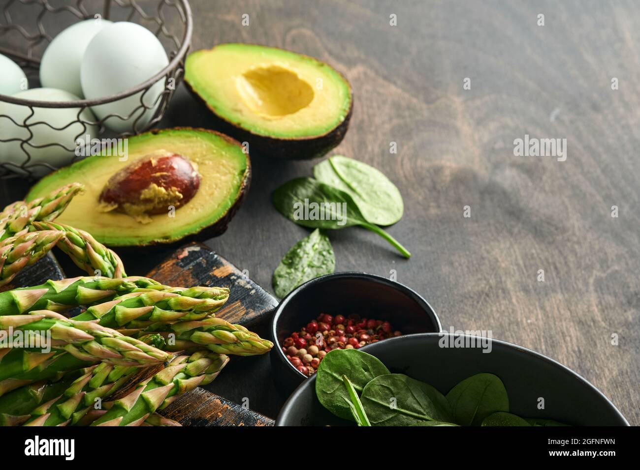 Bunch of fresh green organic asparagus spinach, avocado, chicken eggs and pepper seasoning on black old wooden background, top view. Food cooking back Stock Photo
