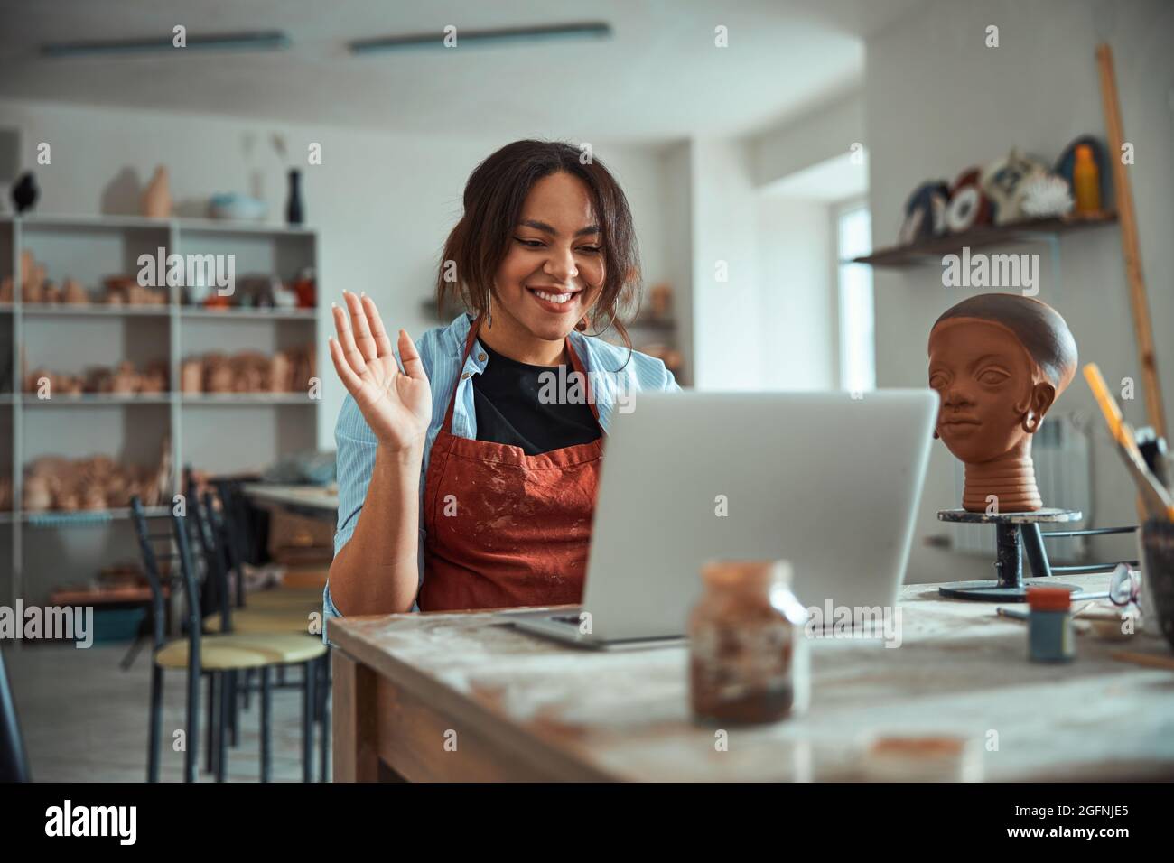 Cheerful female potter using laptop in pottery workshop Stock Photo