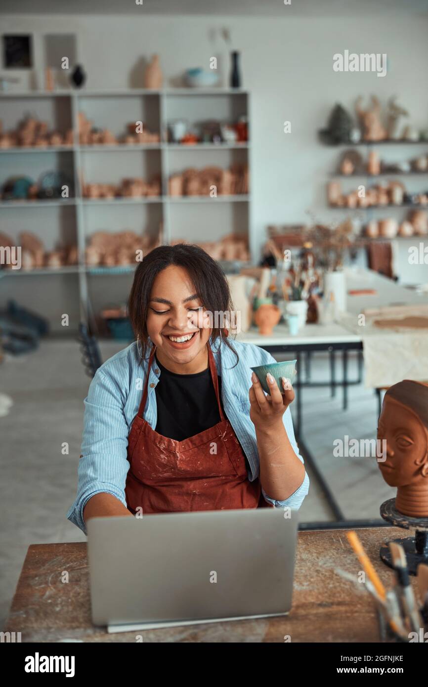Joyful female potter using notebook in pottery workshop Stock Photo