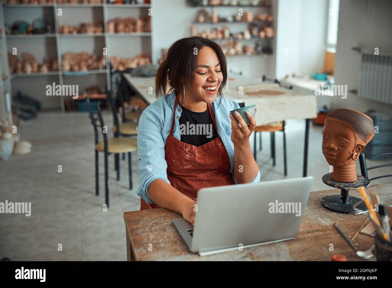 Cheerful female potter using notebook in pottery workshop Stock Photo