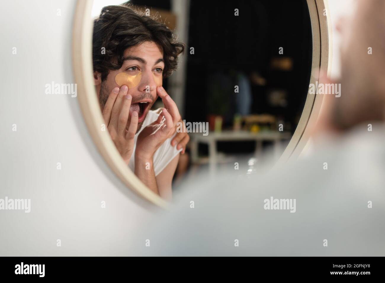 homosexual man applying eye patches and looking at mirror Stock Photo