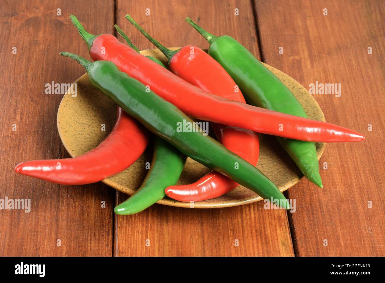 Pods of red and green chili peppers lie strewn on a brown ceramic plate ...