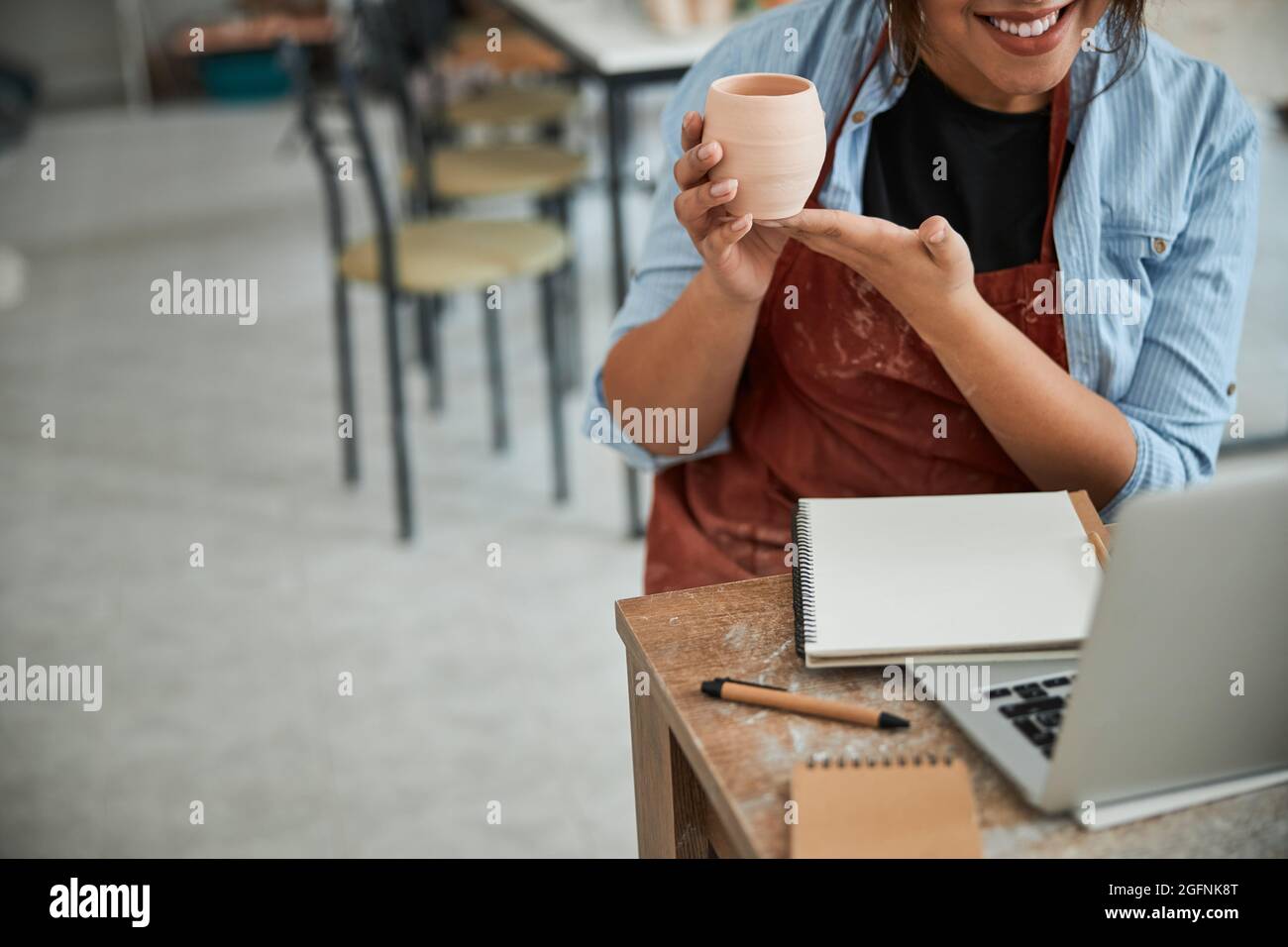 Joyful female potter using laptop in pottery workshop Stock Photo