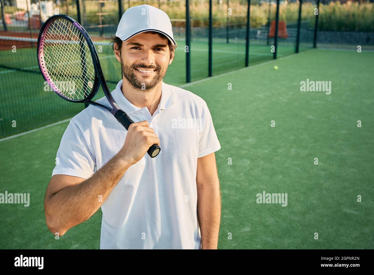 Portrait of a handsome tennis player with a racket in hand standing on a  tennis court wearing a white uniform Stock Photo - Alamy