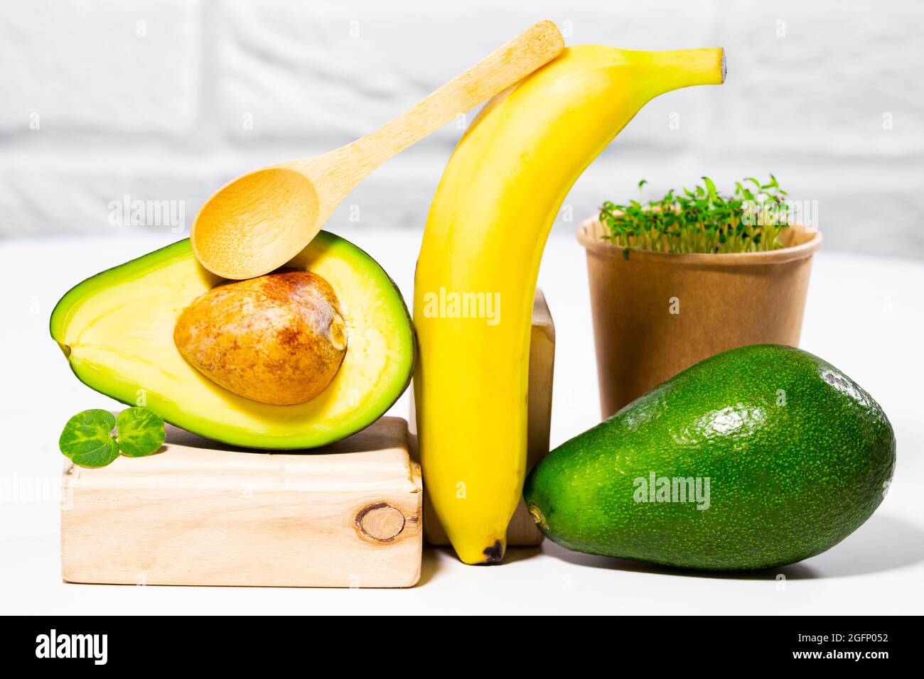 Creative still life with avocado, banana and micro green on whithe backgroun with wooden stands and podiums. Equilibrium healthy food. Balanced nutrit Stock Photo