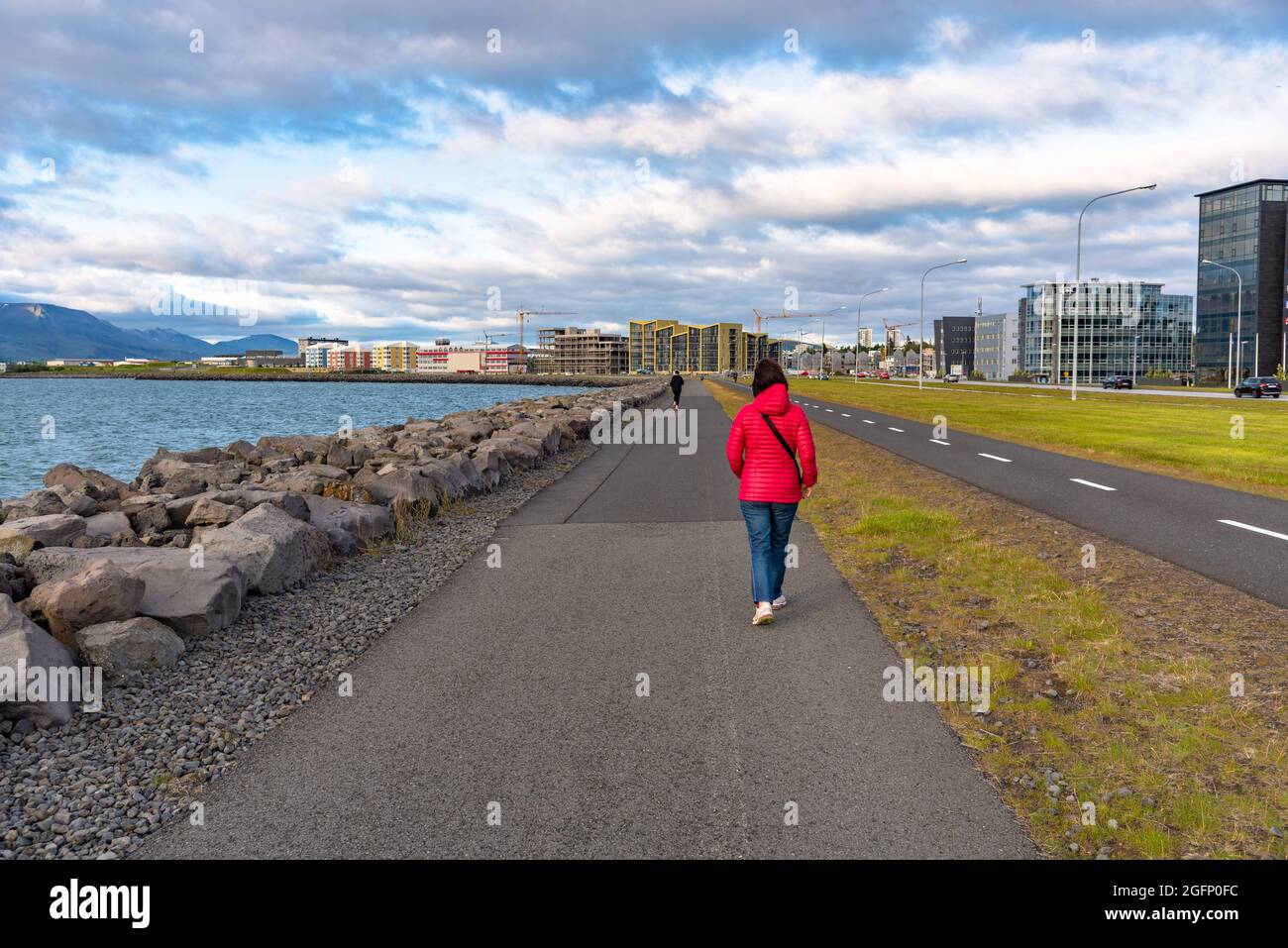 Woman walking on a waterfront footpath on a cloudy summer evening Stock Photo