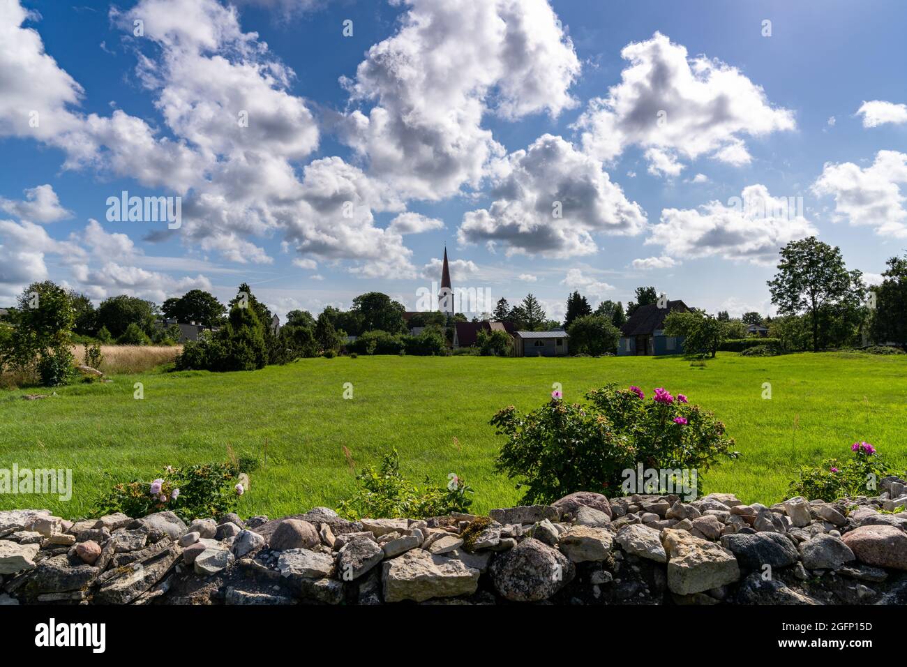Kihelkonna, Estonia - 14 August, 2021: village of Kihelkonna with church steeple and a rock wall and field in the foreground Stock Photo