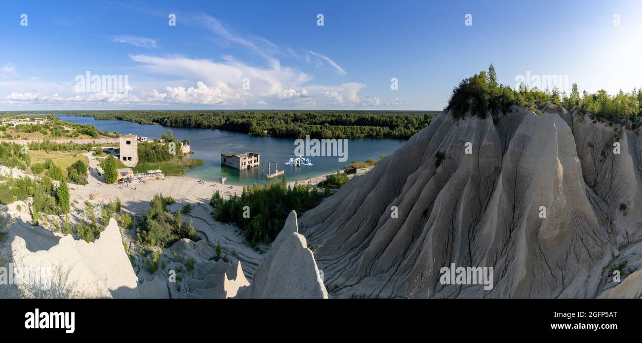 Rummu, Estonia - 12 August, 2021: limestone mountains and calm blue groundwater lake in an old quarry with abandoned buildings in the water Stock Photo