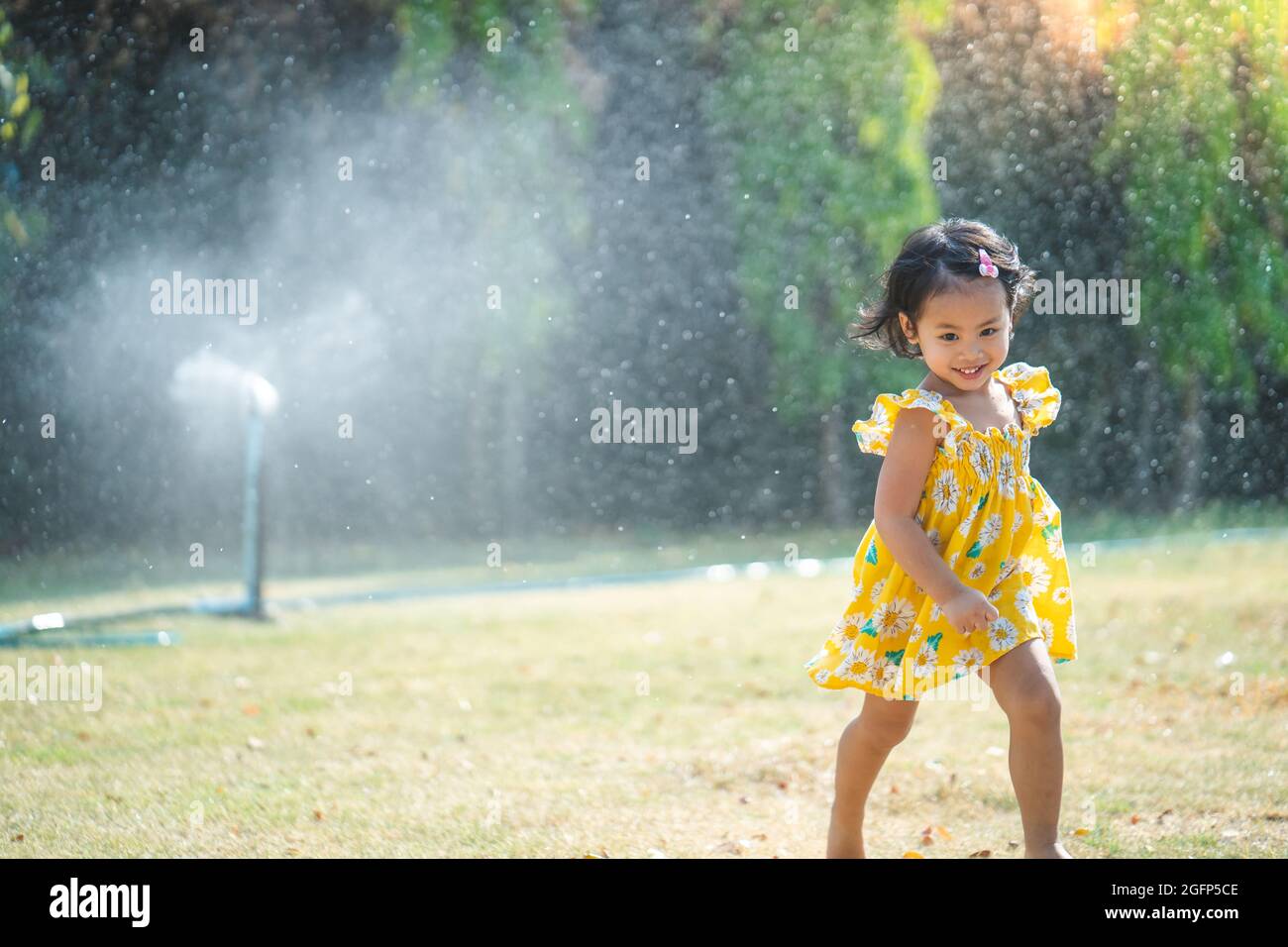 Adorable little Asian girl in a yellow dress playing in the garden with ...