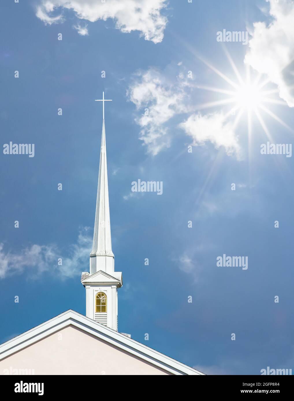 Tall white church steeple with cross on top aganist a blue sky with ...