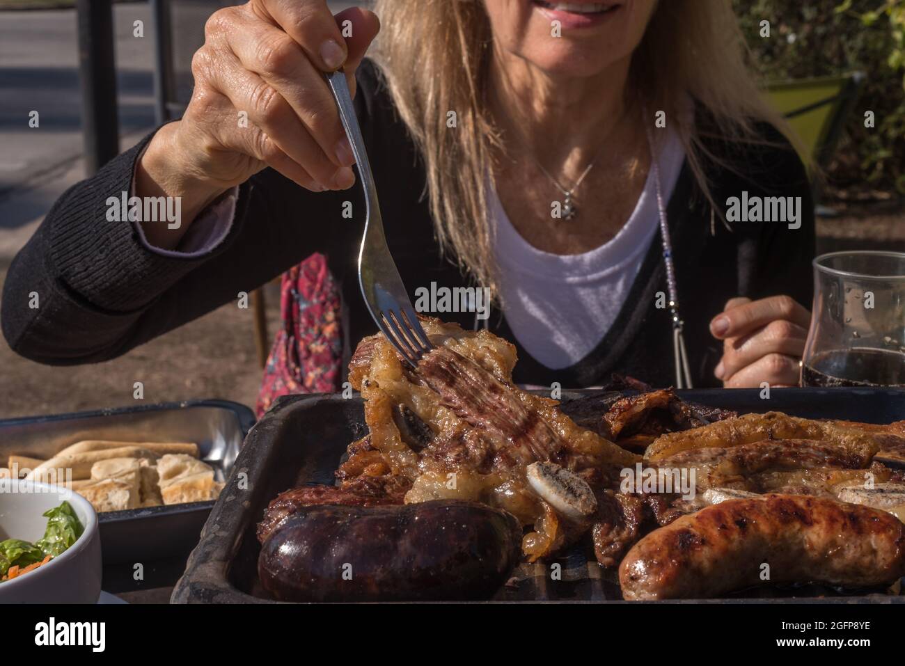 Adult woman skewering a beef grill with fork from an Argentinian barbecue. Horizontal photograph. Stock Photo