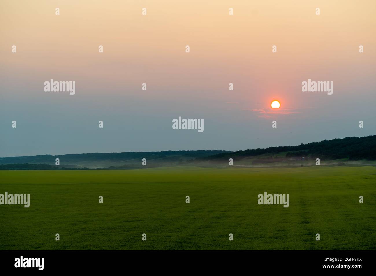 Scenic shot of a green meadow surrounded by forest mountains under the ...