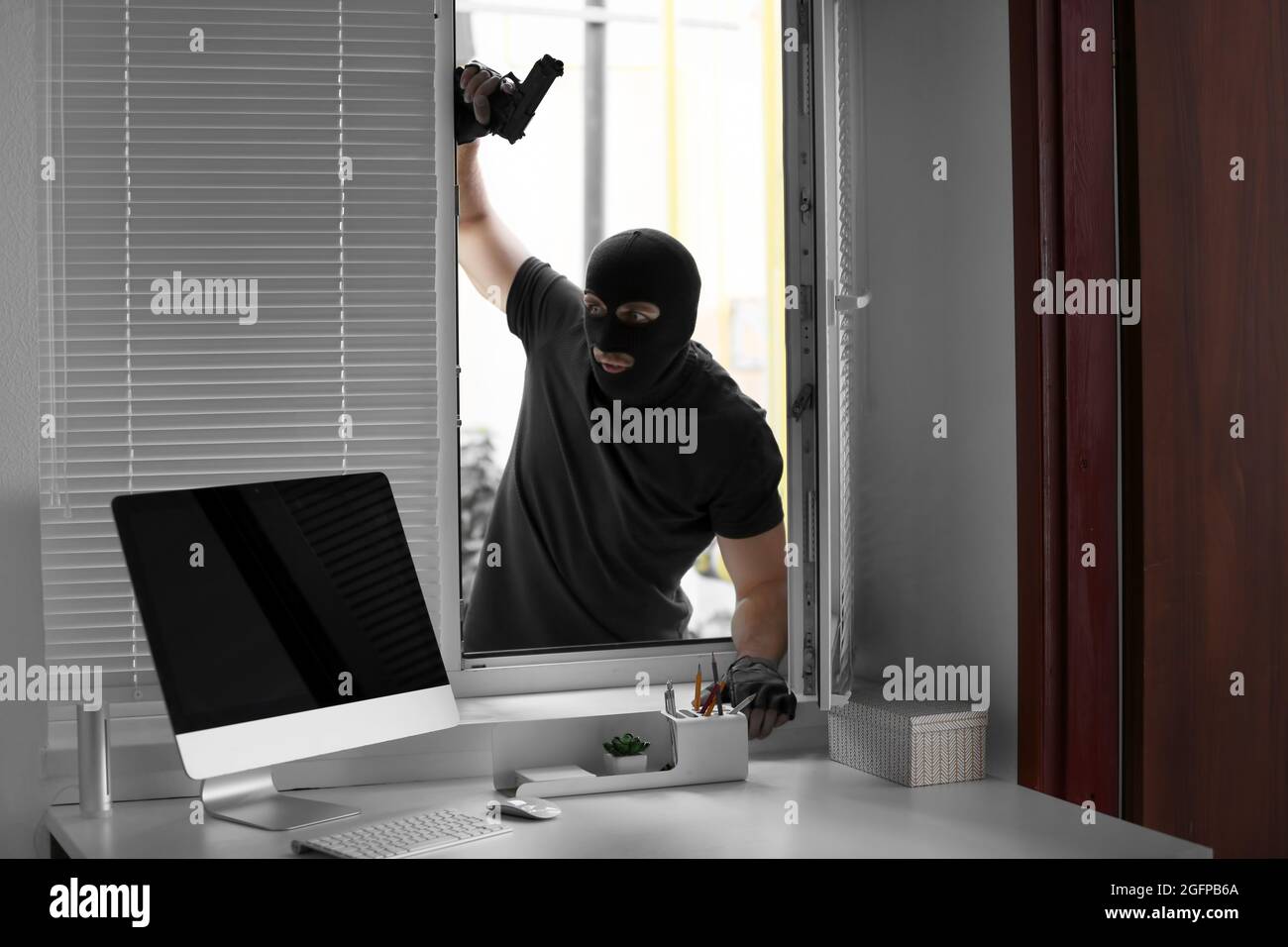 Thief with gun entering office through window Stock Photo - Alamy