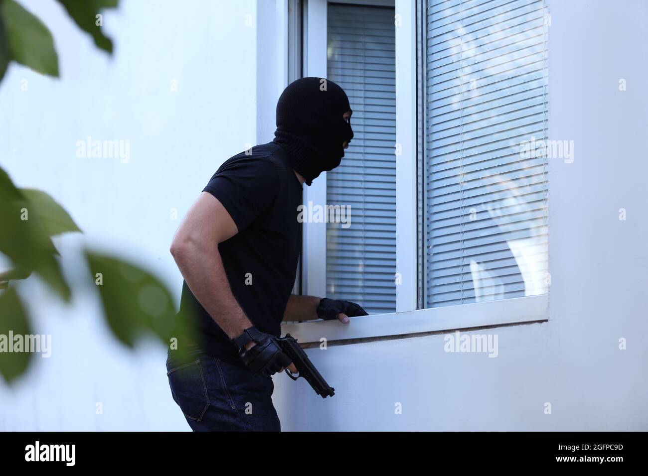 Thief with gun entering house through window Stock Photo - Alamy