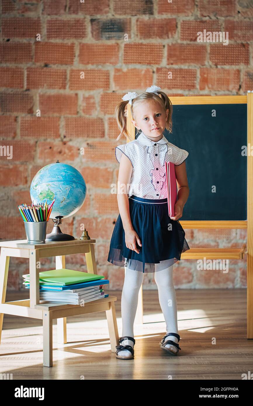 Cute little girl in school uniform posing next to school board with book  Stock Photo - Alamy