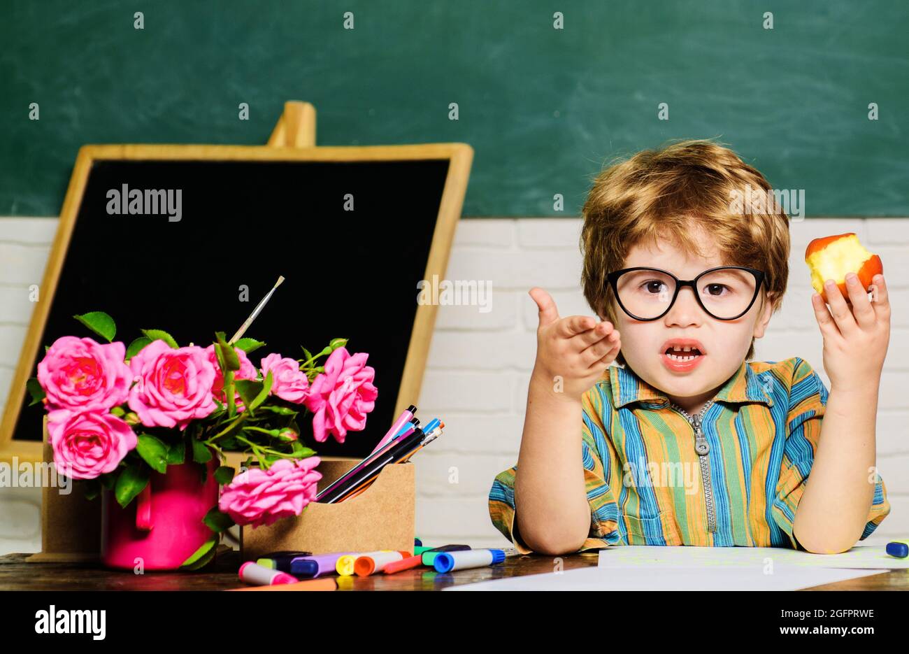 School boy having lunch with apple. Healthy food for children. Little pupil during lunch break in classroom. Stock Photo