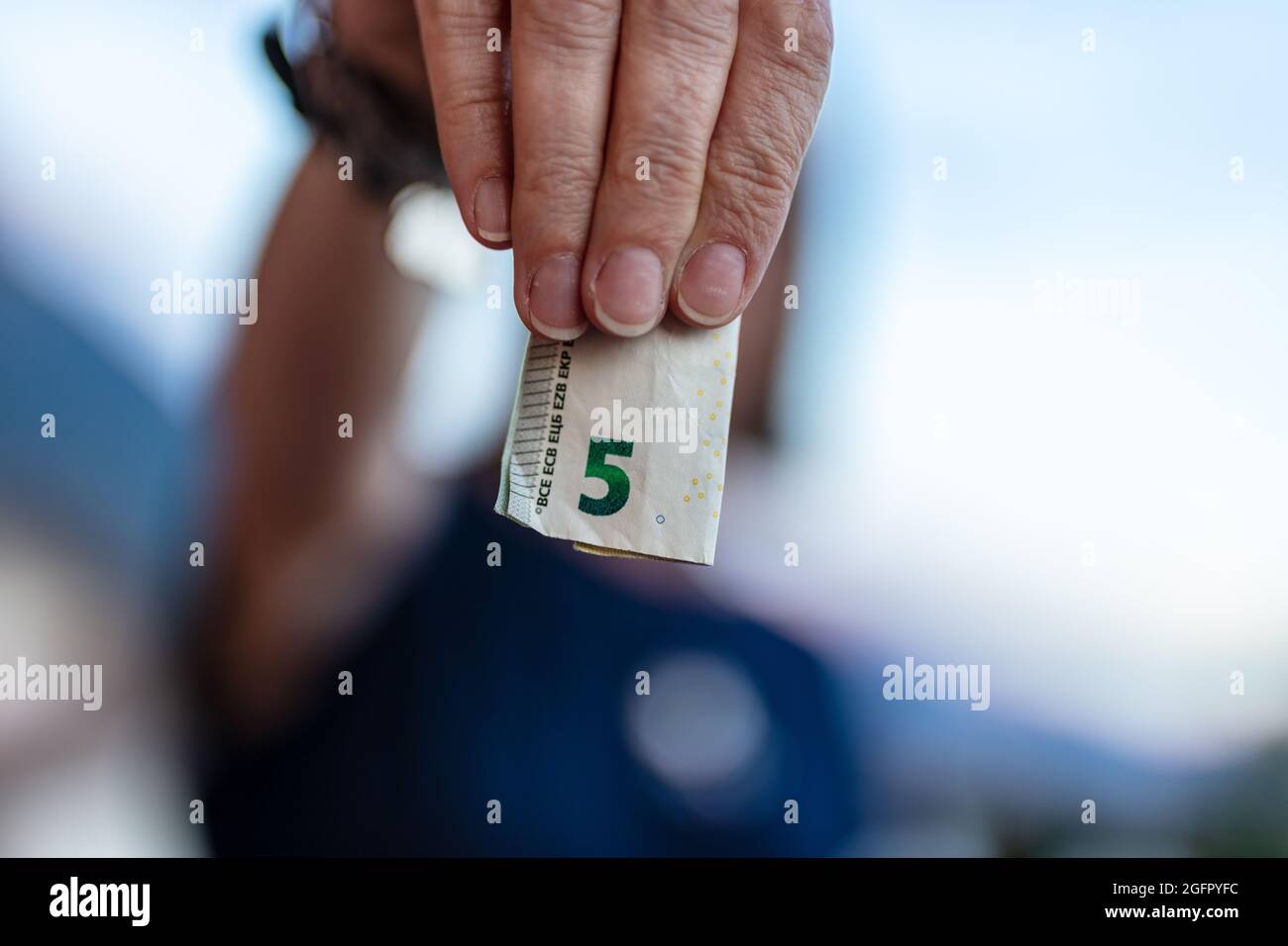 five euro in cash, focus on a folded European currency, held by four unrecognizable person's finger, shallow depth of field on the body in background Stock Photo