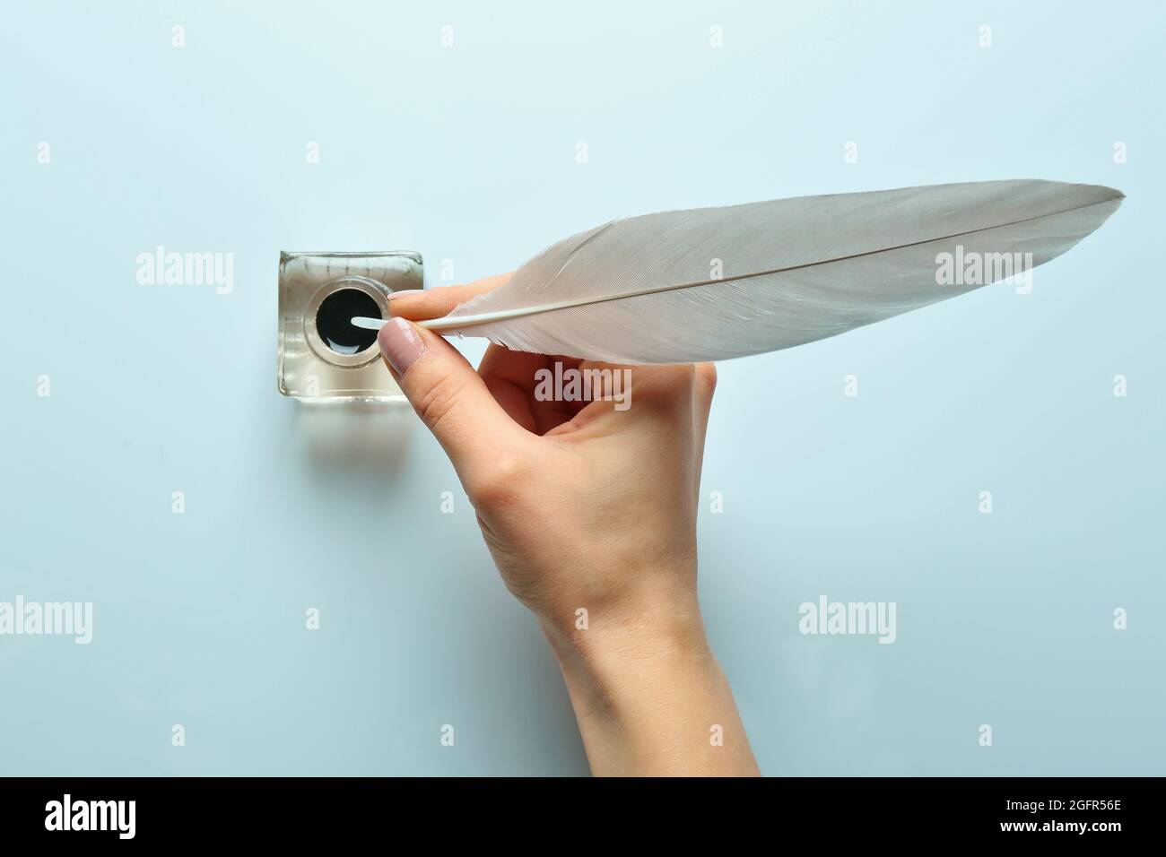 Female Hand Dipping Feather Pen Into Inkwell On Light Background Stock