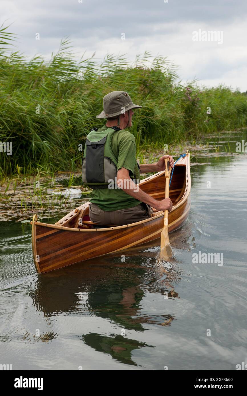 Man paddles a wooden Canadian Cedar Strip Canoe down a still river in