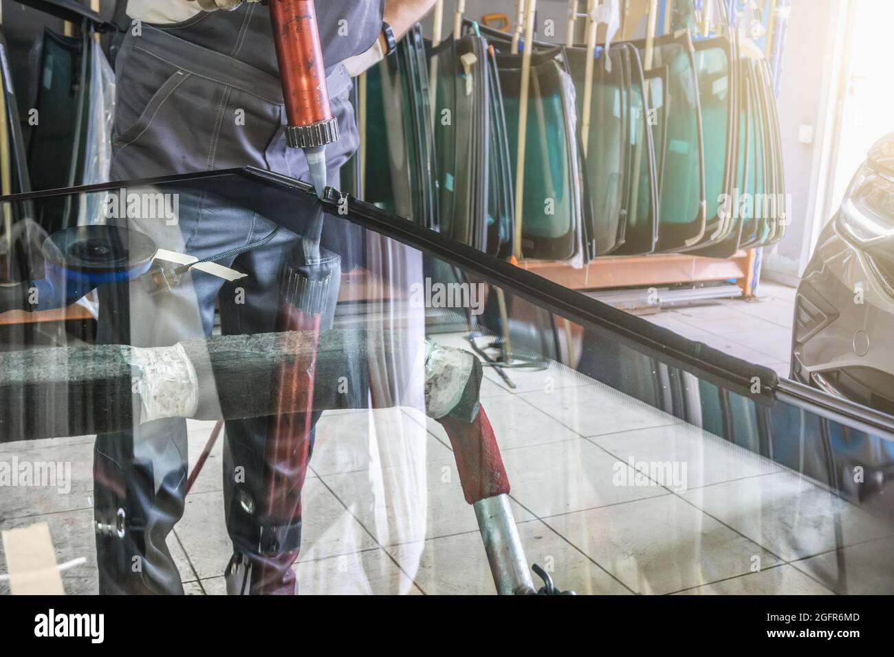 Process of preparing windshield for replacement in car service. Worker applies special adhesive sealant to windscreen before installation on auto. Stock Photo