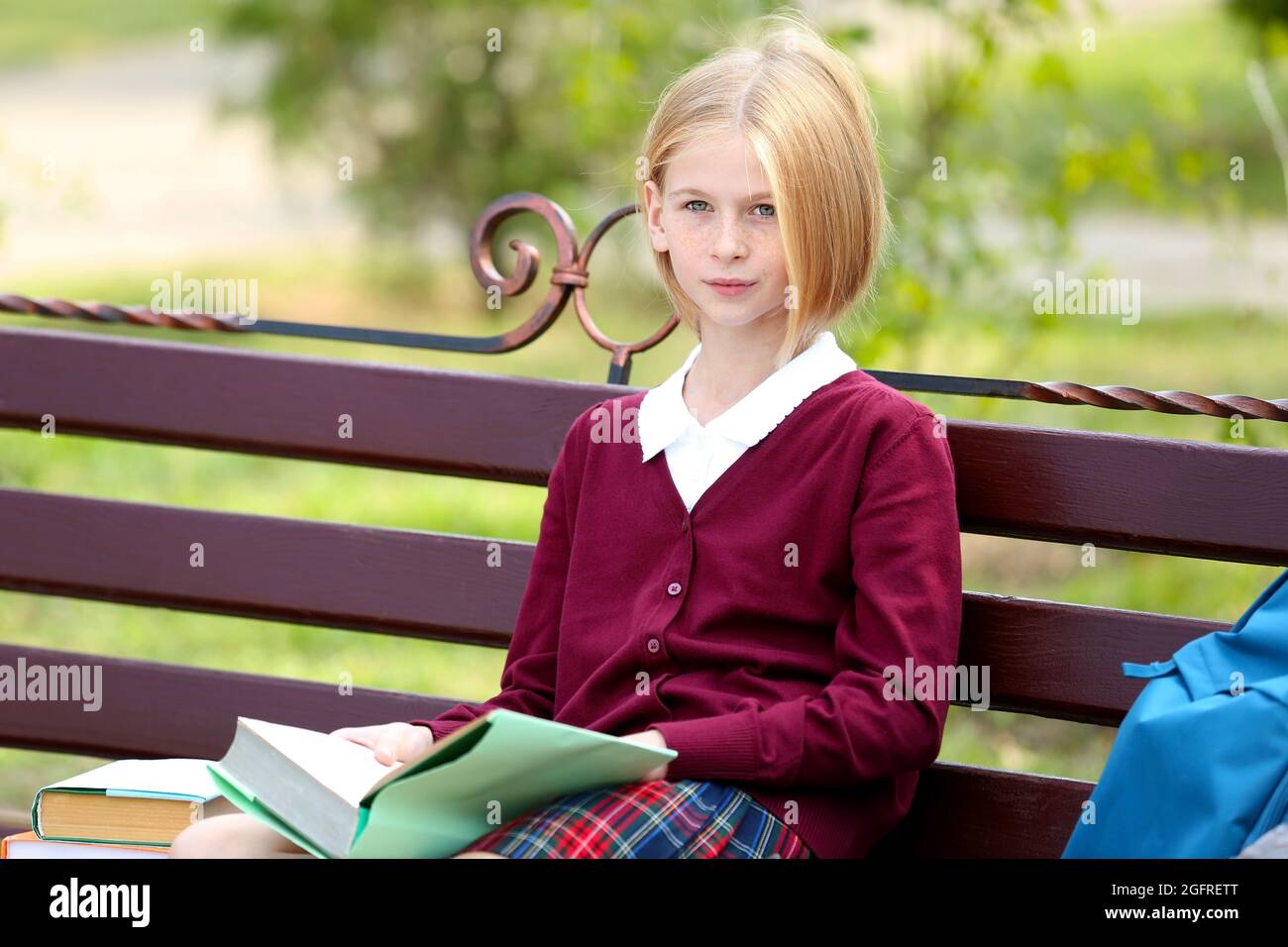 Schoolgirl reading book while sitting on bench in park Stock Photo - Alamy