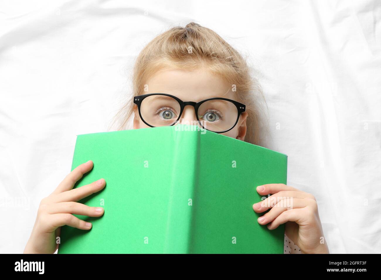 Funny little girl lying on bed with book Stock Photo Alamy