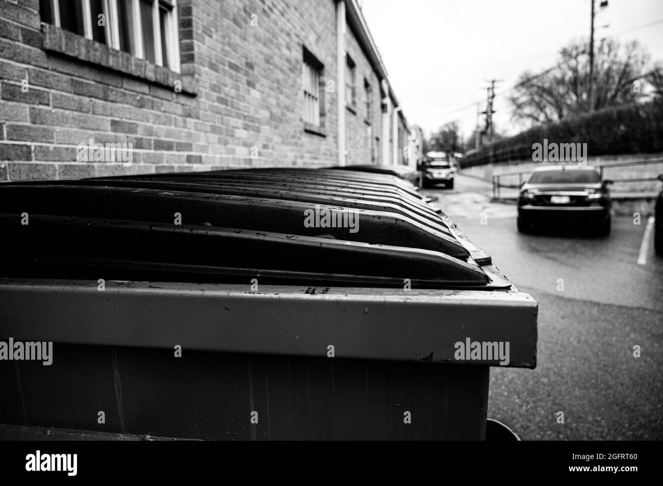 row of covered garbage bins along a brick wall in a back alley Stock Photo