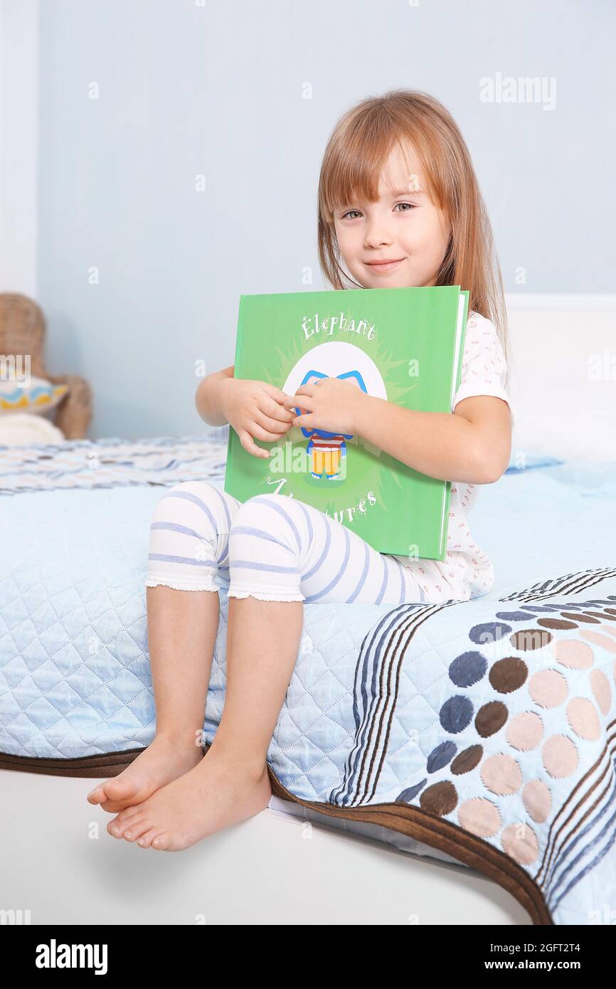 Little cute girl sitting with book on bed Stock Photo - Alamy
