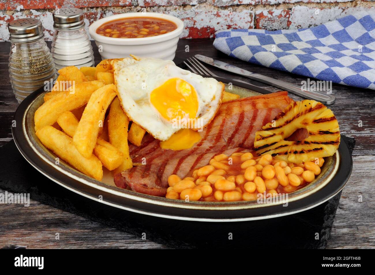 Grilled gammon egg and chips meal with baked beans and pineapple fruit ring Stock Photo