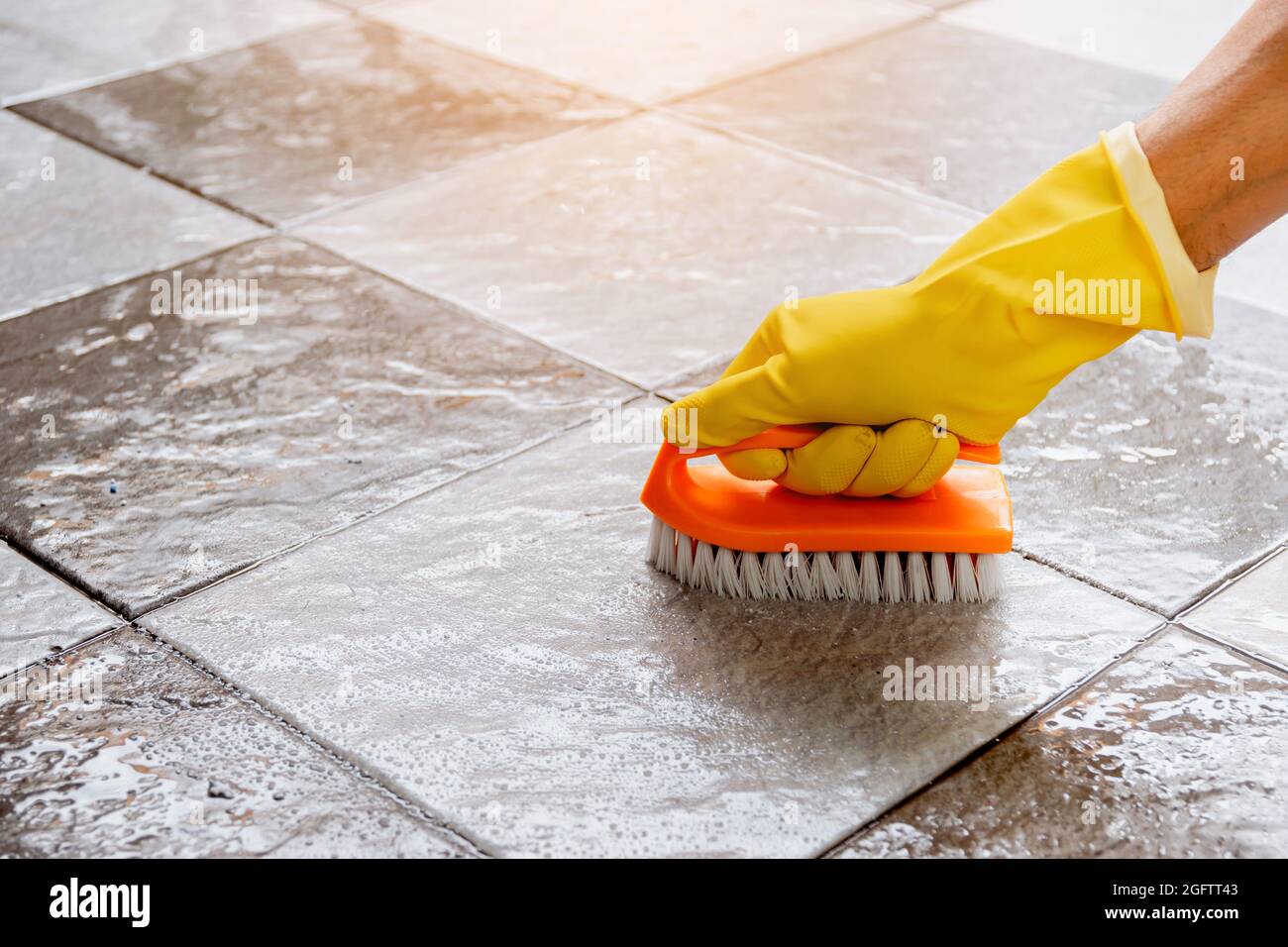 Hands wearing yellow rubber gloves are using a plastic floor scrubber to  scrub the tile floor with a floor cleaner Stock Photo - Alamy