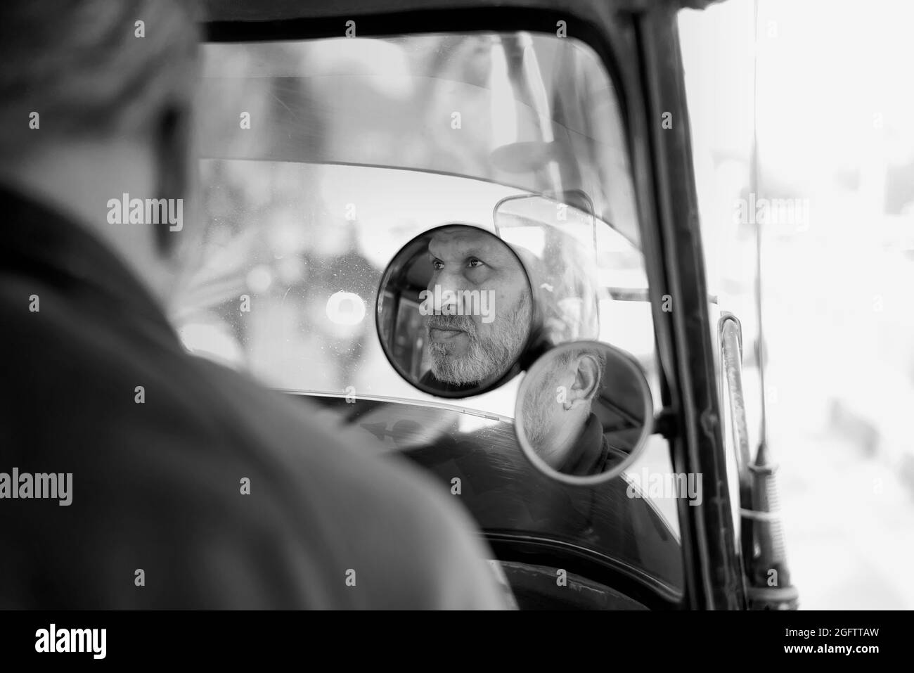 Black and white street photograph of an old Auto Rickshaw driver and his reflection in the mirror Stock Photo
