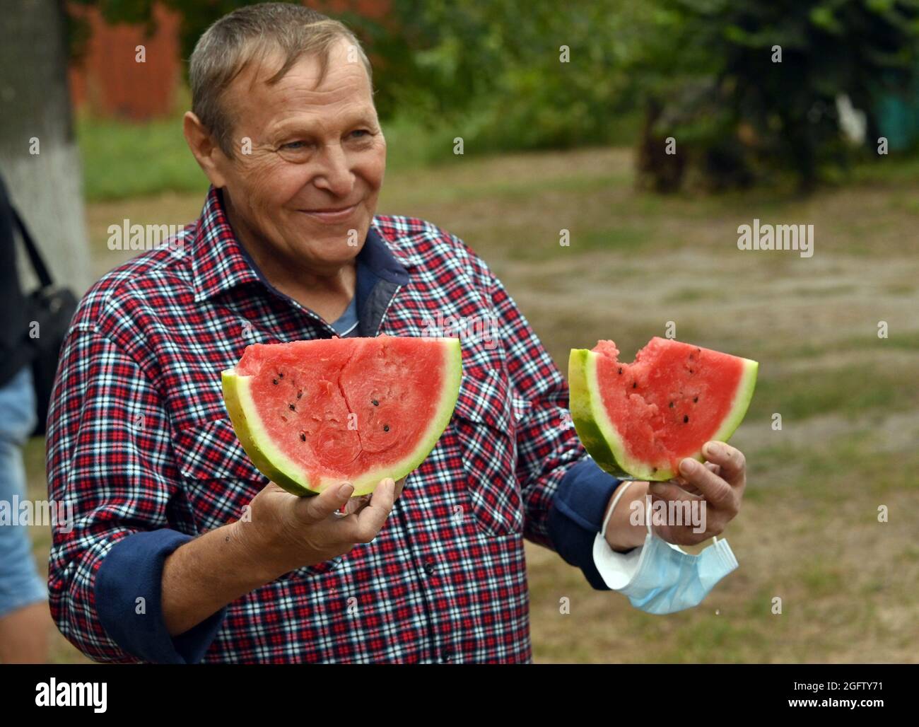 SIEVIERODONETSK, UKRAINE - AUGUST 24, 2021 - A man in a checked shirt holds two slices of a watermelon during the Bashtan Fest, a watermelon festival Stock Photo