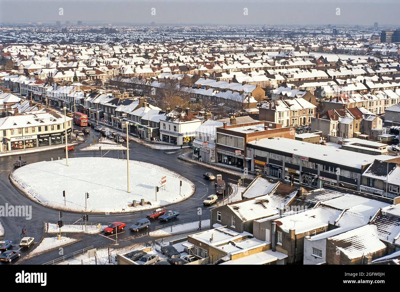 Archive 1991 winter sunshine in aerial view of treated road traffic roundabout junction at Fanshaw Lane and Longbridge Road with snow covered 1990s housing roof tops beyond in this densely populated 90s archival image of an urban landscape in the town of Barking in East London England UK Stock Photo
