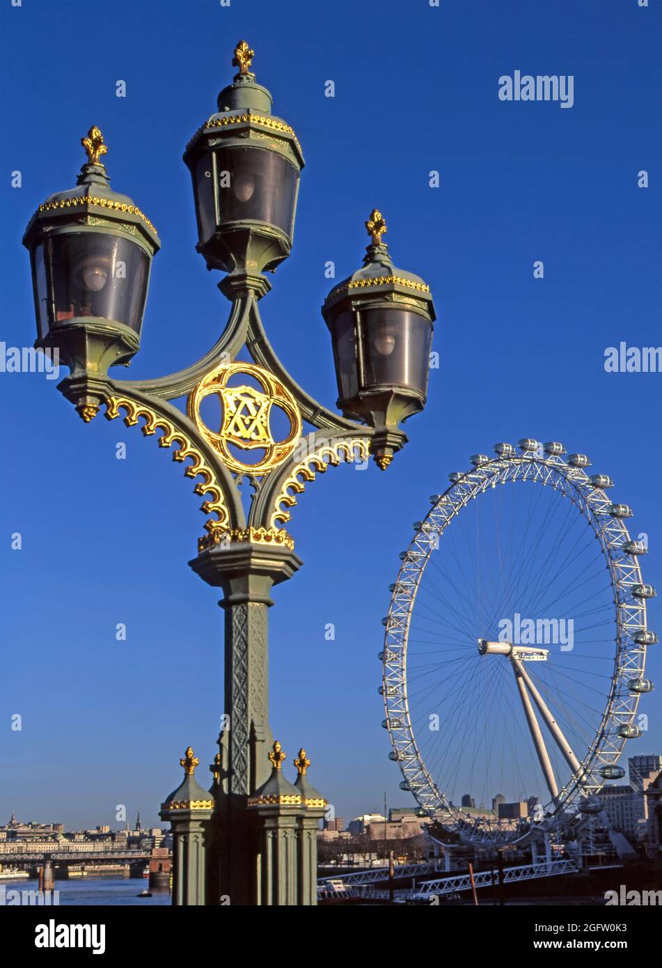Ancient and modern archive 1999 view of the London Eye ferris wheel in position ready for its ceremonial opening for the new year 2000 millennium celebrations a now famous landmark beyond a close up of historical 1990s archival image of Victorian three cluster street lights on cast iron lamp post column on Westminster road bridge a  comparison of eye-catching riverside structures in London England UK Stock Photo