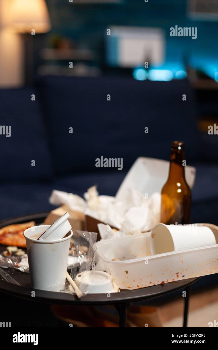 Chaotic home of lonely person with sever mental health problem having rubbish on messy table with with beer bottles and food leftover. Empty living room of depressed untidy person with depression Stock Photo