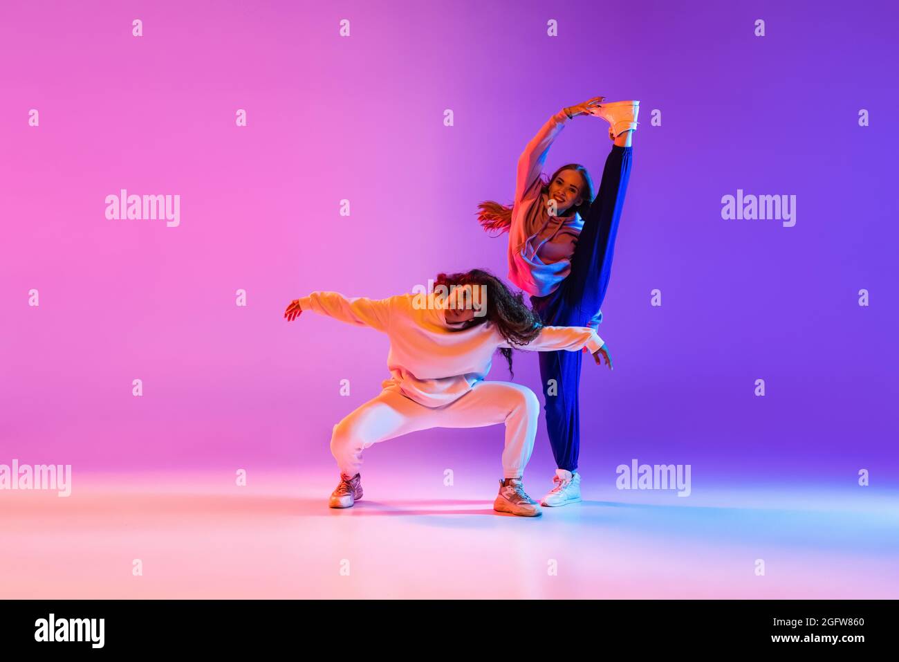 Two beautiful young girls dancing hip-hop on gradient pink purple neon ...