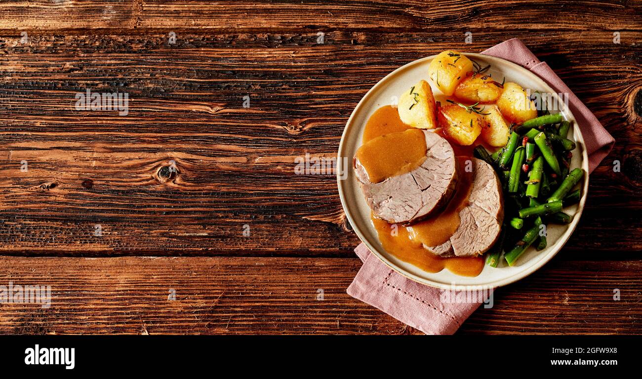 Gourmet tender roast beef medallions with fresh green beans and crispy golden potatoes topped with a spicy gravy served on a plate with napkin on a ru Stock Photo