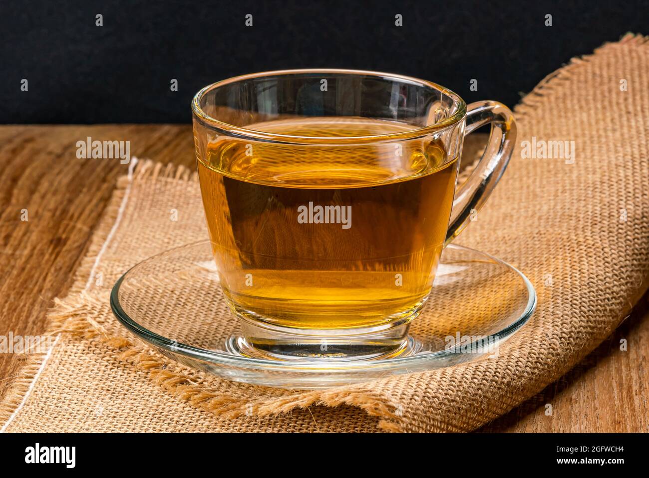 Side view of a cup of hot tea in saucer on sack cloth. Hot tea in a transparent glass on sack cloth. Stock Photo