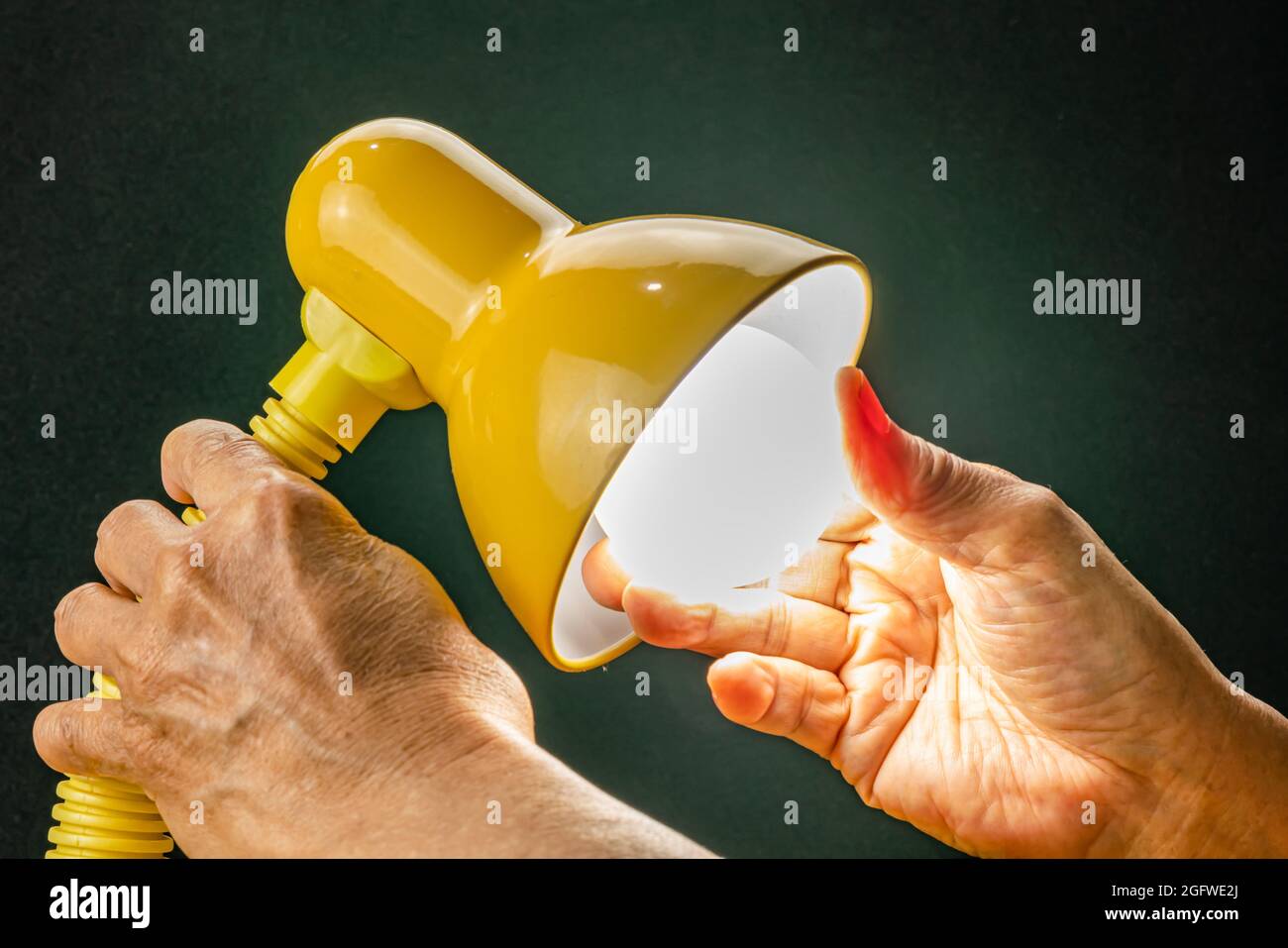 Putting new led light bulb into the socket of desk lamp. Senior hand replaced new light bulb of reading lamp and turning on. Stock Photo