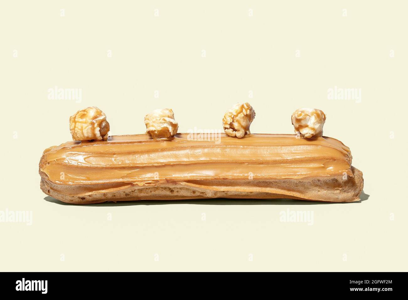 Caramel glaized eclair decorated with popcorn isolated on yellow background Stock Photo