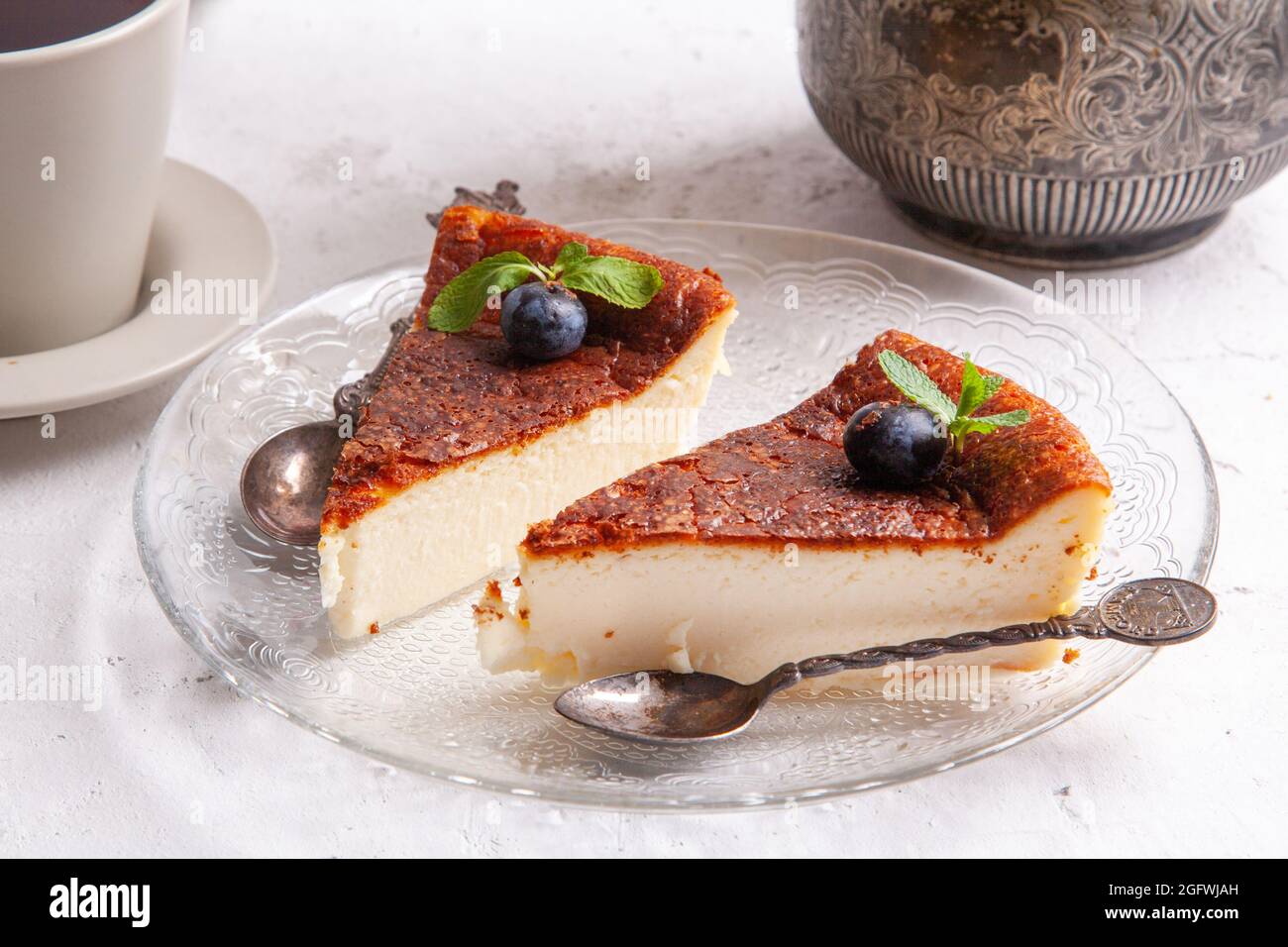 Slice of Homemade Basque burnt cheesecake on a plate with blueberries and  mint leaves on light background Stock Photo - Alamy