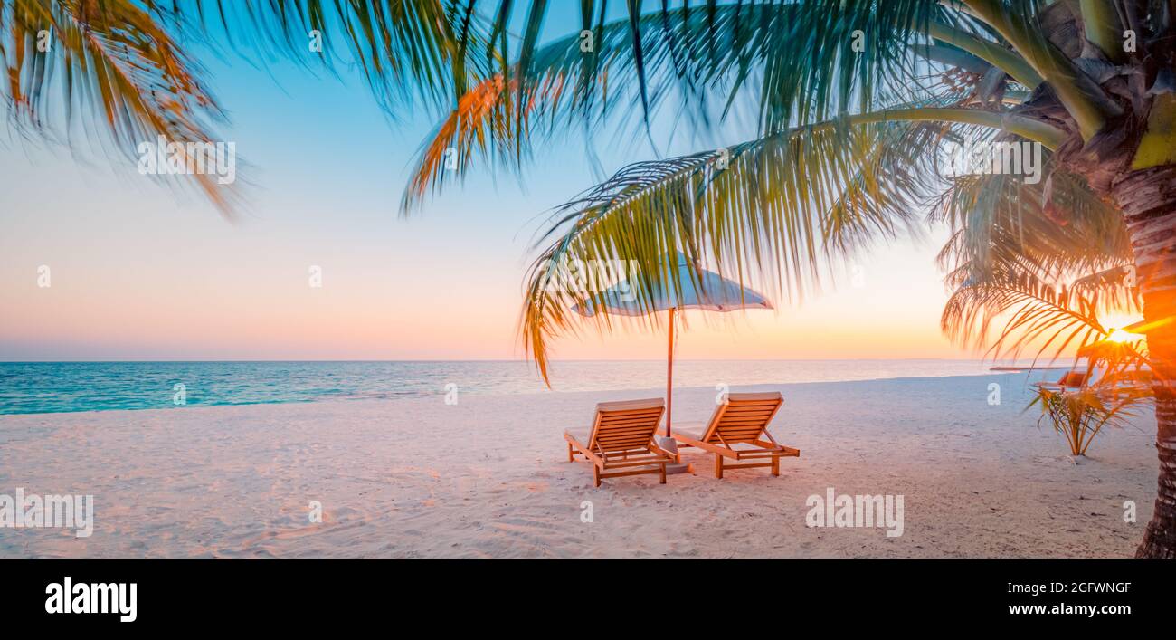 Amazing tropical sunset scenic, two sun beds, loungers, umbrella palm tree leaves. Seaside island horizon, romantic twilight sky. Vacation holiday Stock Photo