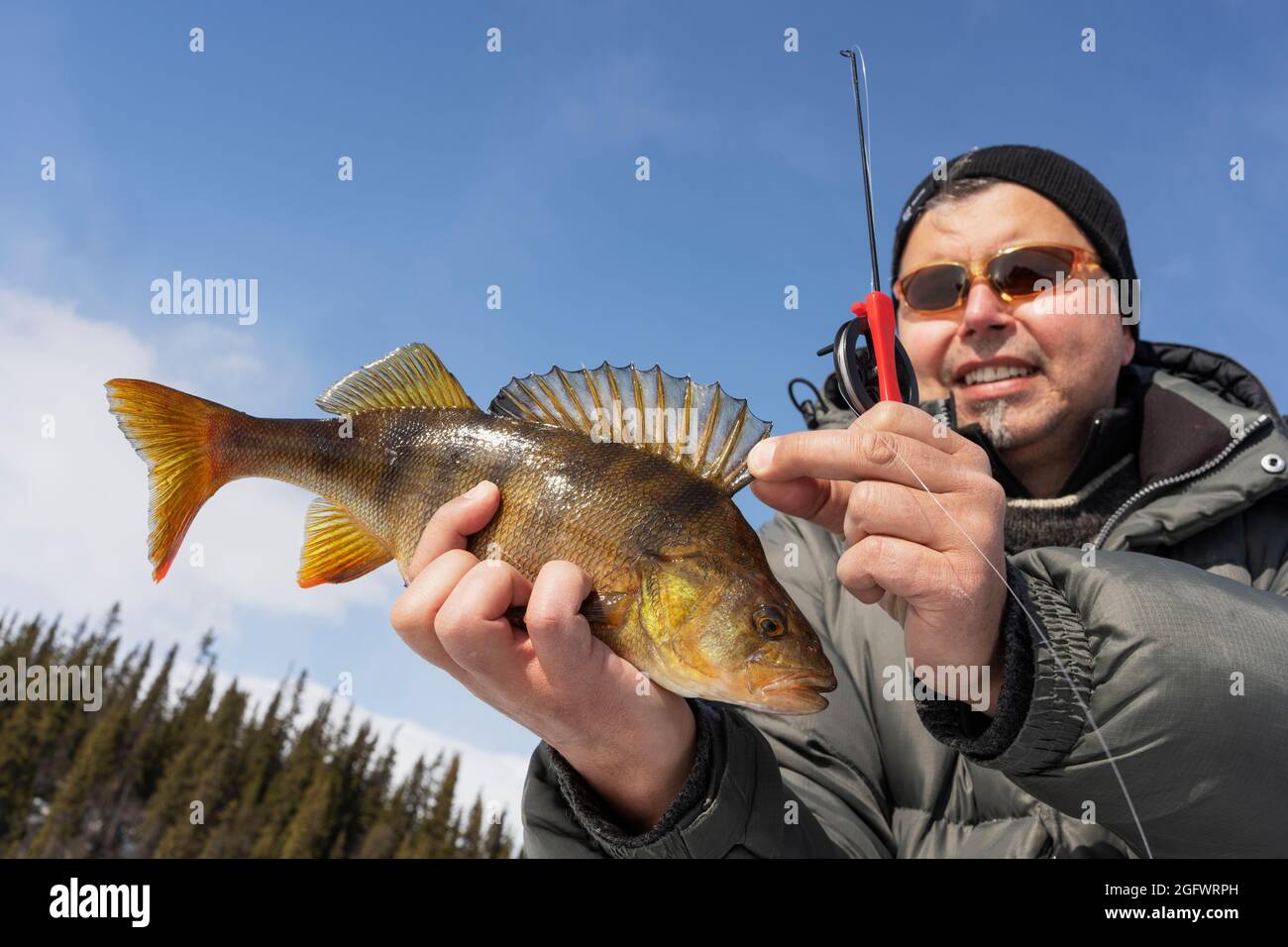 Man ice fishing at sunny day Stock Photo