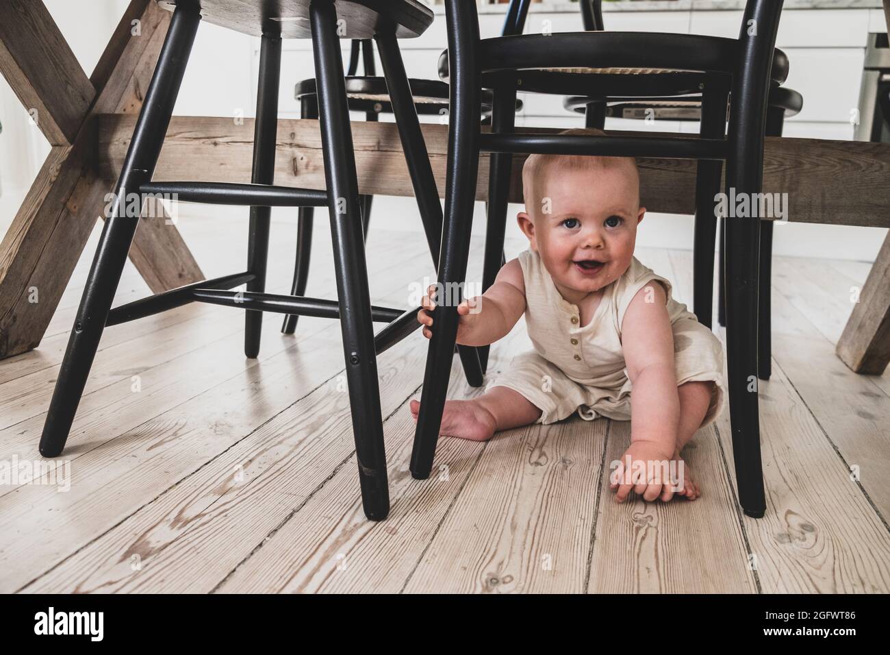 Smiling baby sitting under chair Stock Photo