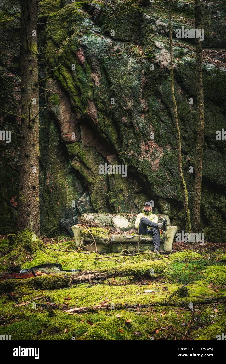 Man sitting on old sofa next to rock wall Stock Photo